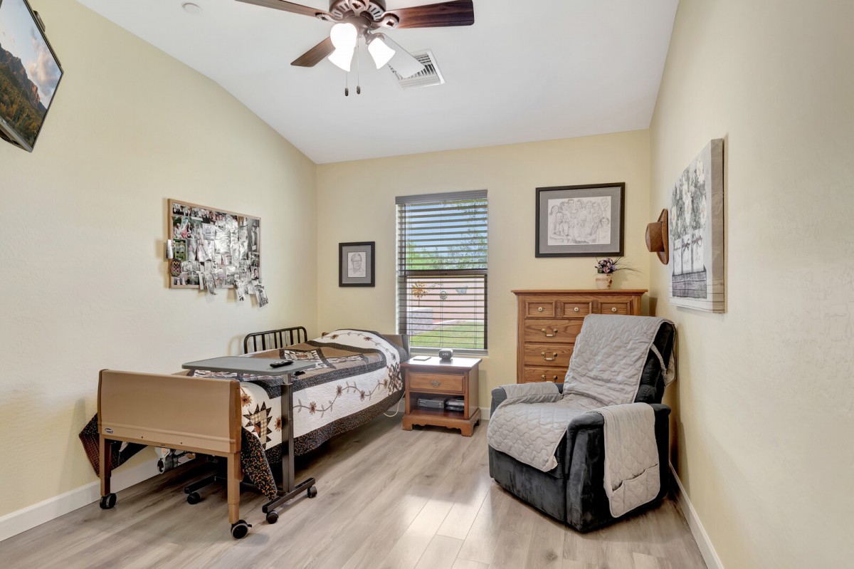 A room with a hospital bed, comfortable chair, and wooden furnishings.