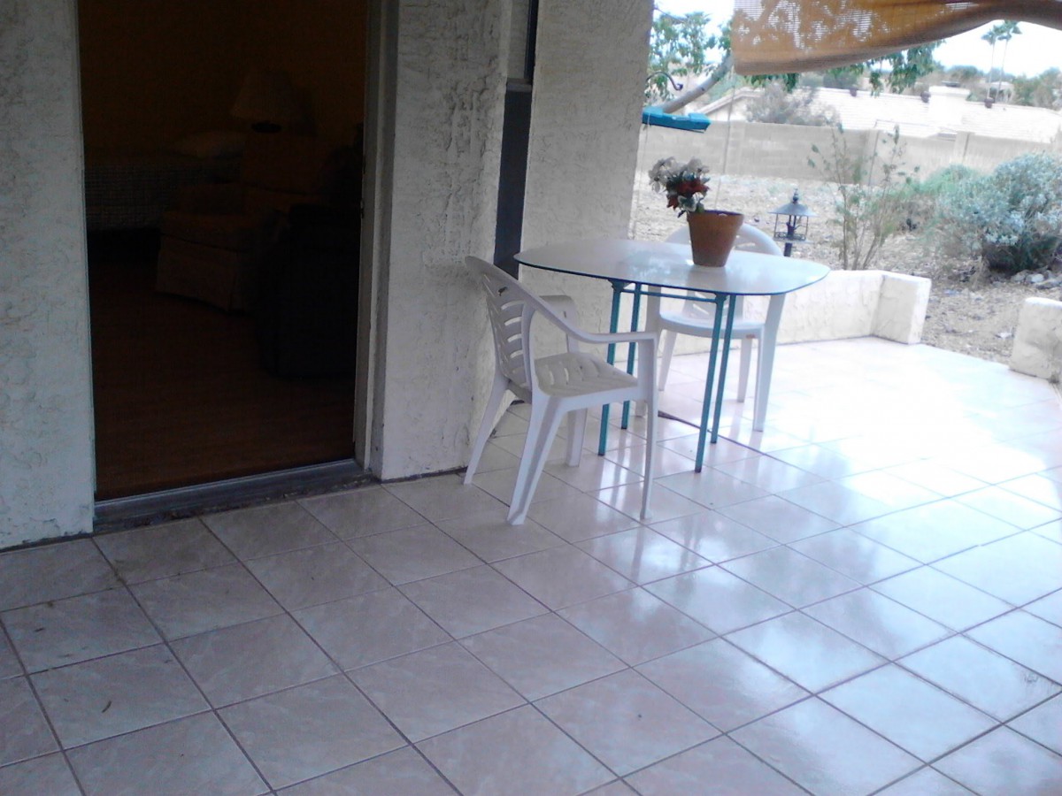 An outdoor patio with a table, a white chair, and a potted plant on a tiled floor.