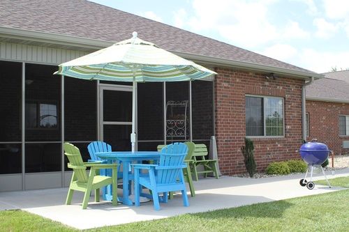 A patio with colorful chairs and a table under a striped umbrella next to a brick house.
