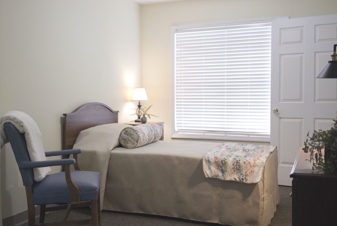 A cozy bedroom with a single bed, lamp, and window blinds.