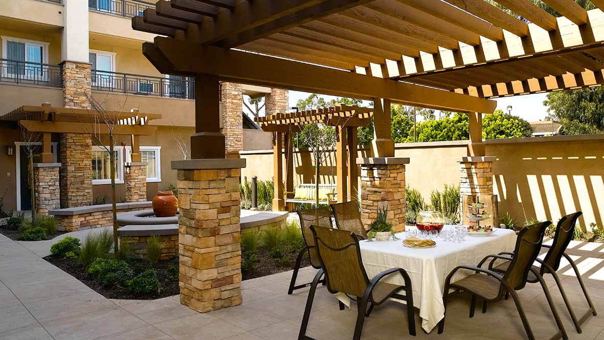 A beautifully set outdoor patio with a pergola, featuring a dining table and stone columns.