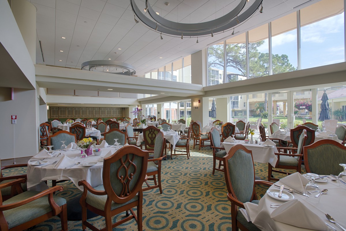 An elegant dining room with tables and chairs, featuring large windows allowing natural light to fill the space.