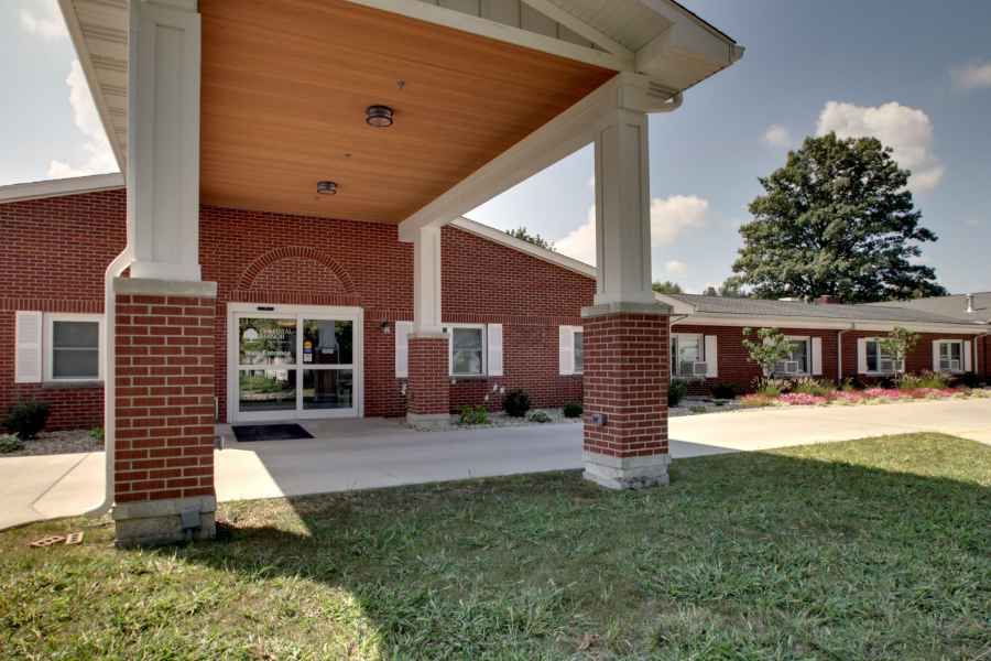 A brick building entrance with columns and a landscaped lawn.