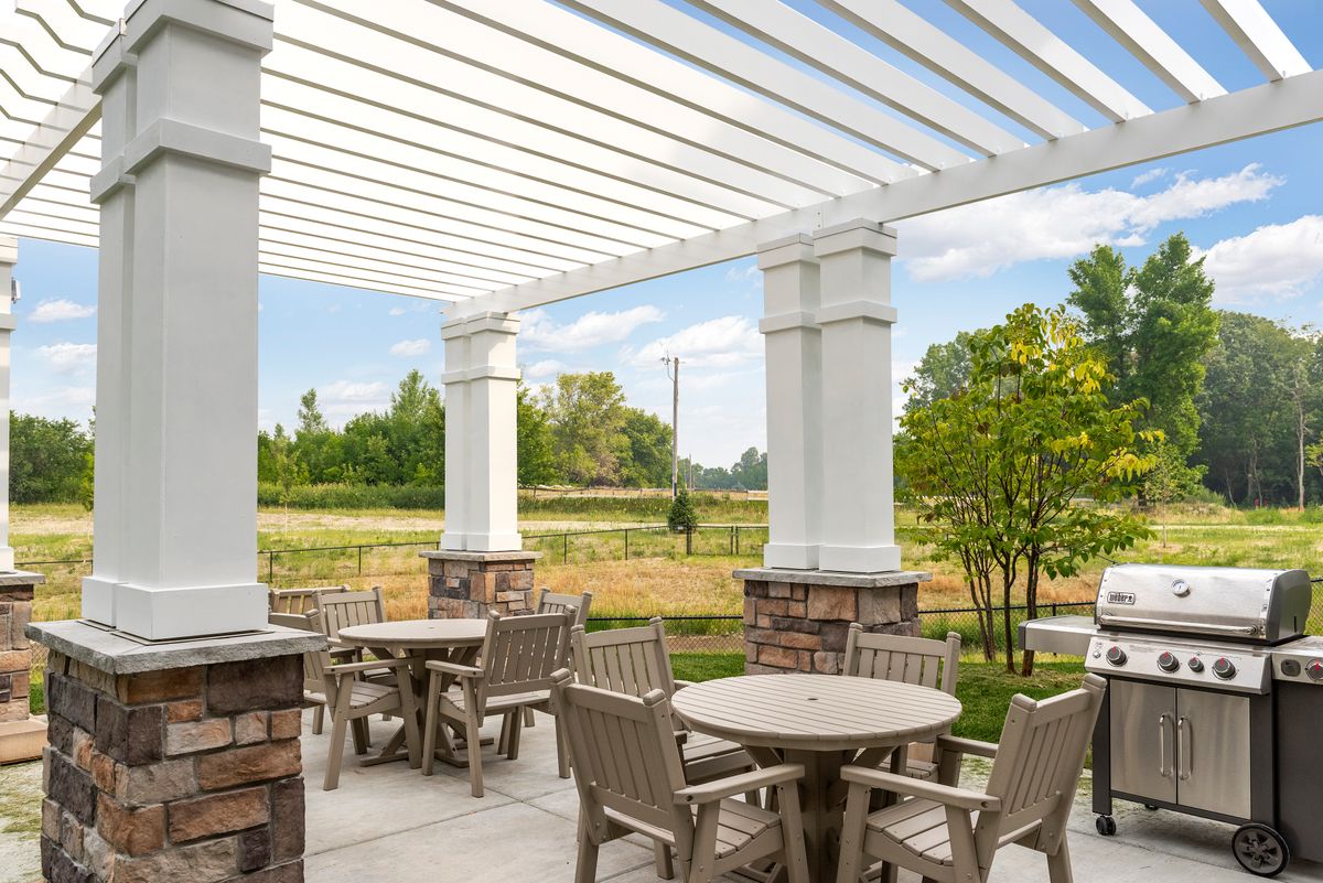 A serene outdoor seating area with tables and chairs under a pergola, surrounded by nature.