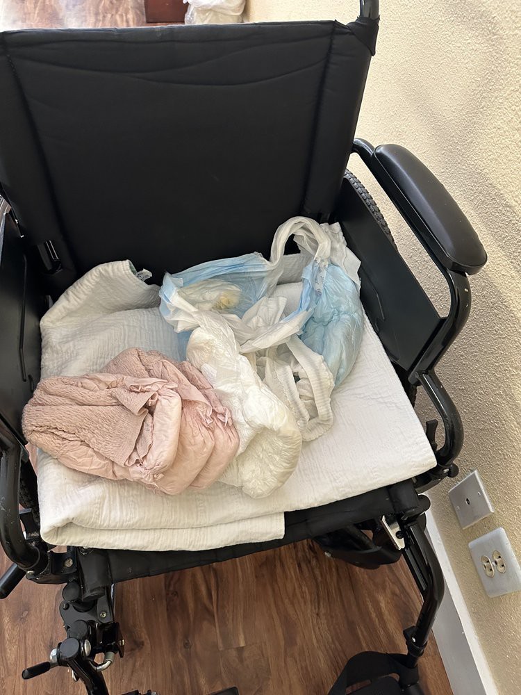 A wheelchair with clothing and a bag placed on its seat indoors.