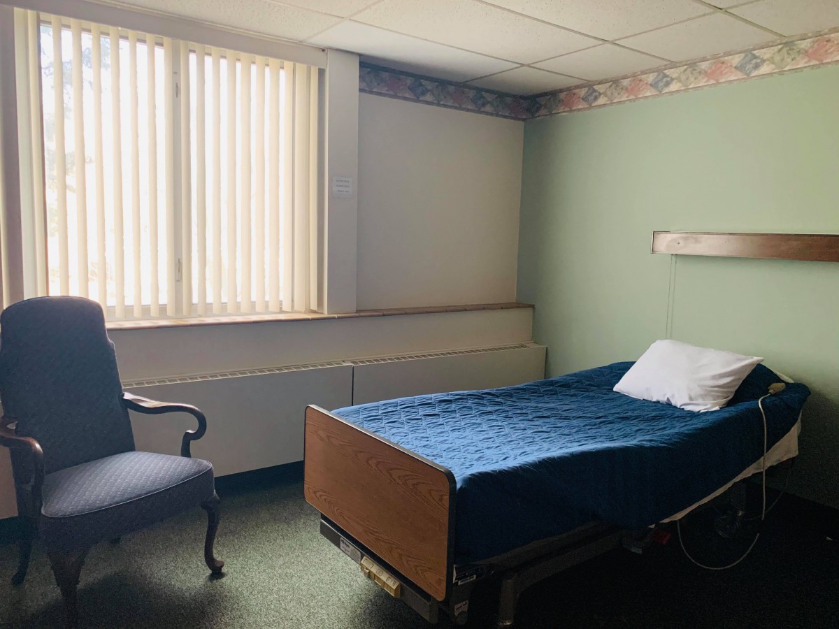 An empty hospital room with a bed and a chair by the window.