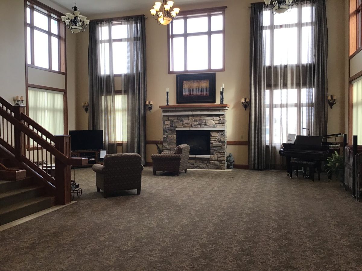 Spacious living room with a fireplace and high windows, featuring comfortable seating and a piano.