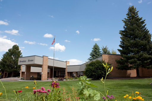 A school building with a flagpole, surrounded by flowers and trees under a clear blue sky.