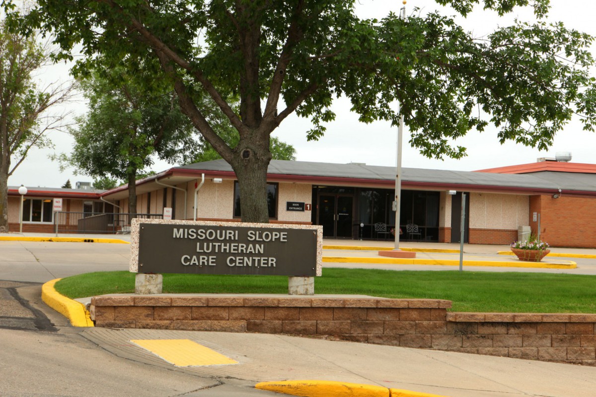 The exterior of the Missouri Slope Lutheran Care Center with a visible sign and surrounding trees.