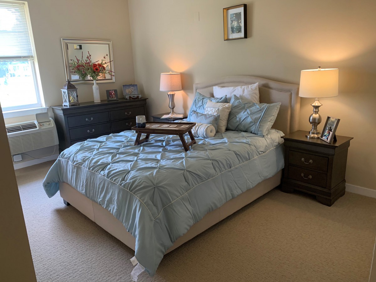 A cozy bedroom with a neatly made bed, bedside tables, and soft lighting from lamps.