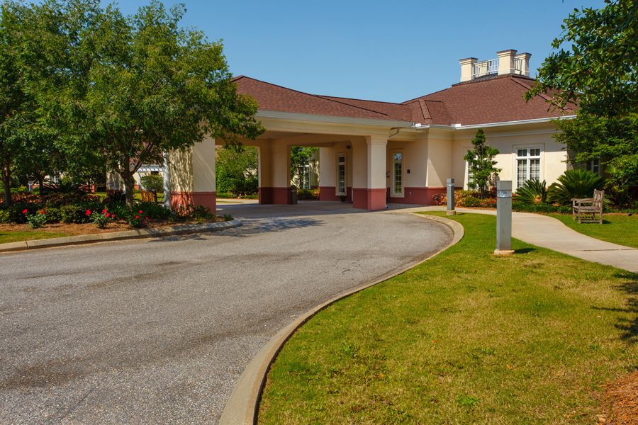 A curved driveway leads to a building entrance surrounded by trees and landscaping.