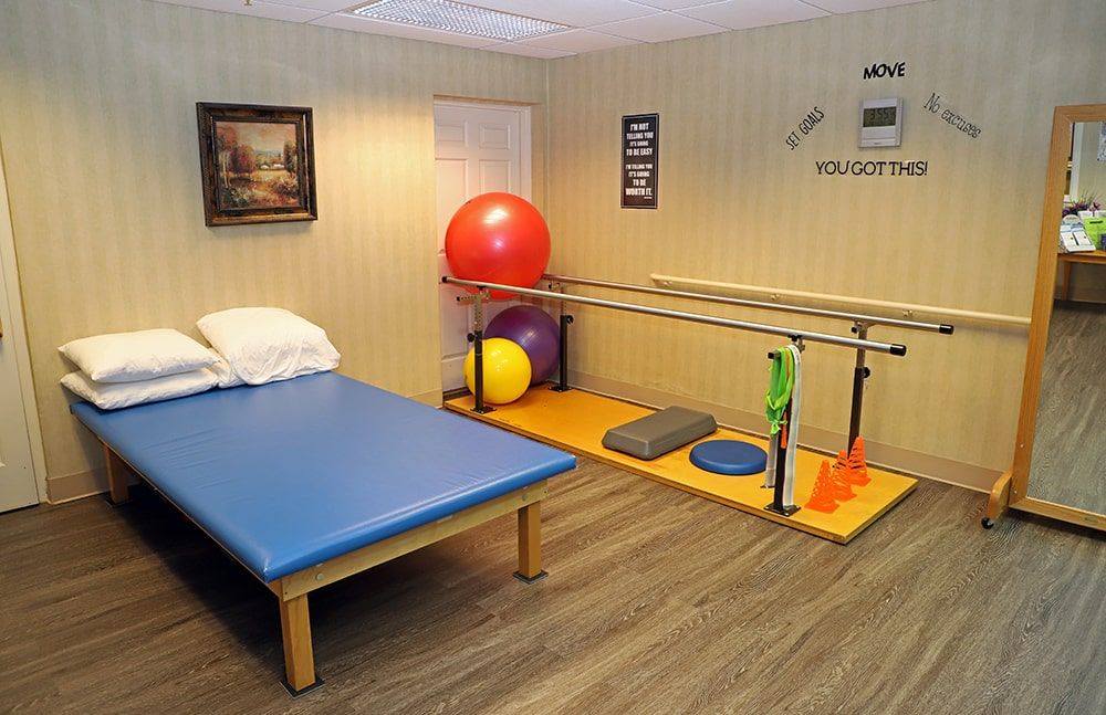 A well-equipped rehabilitation room featuring a therapy bed, gym balls, and parallel bars for physical therapy exercises.