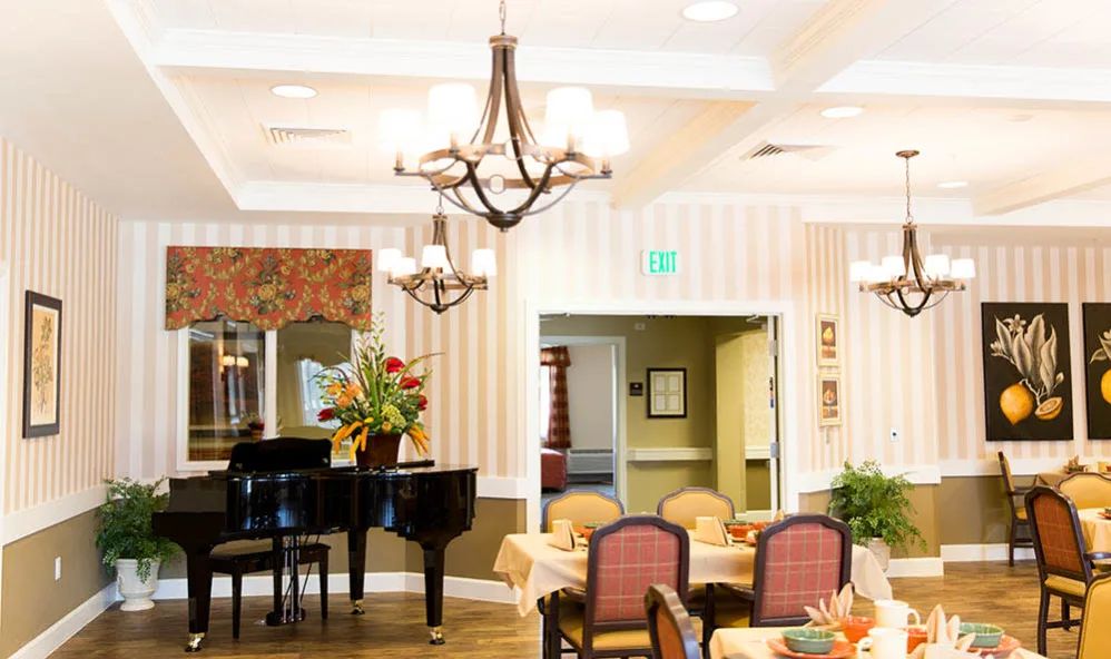 A well-decorated dining area featuring a grand piano, elegant chandeliers, and floral arrangements.