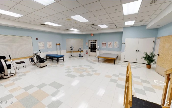 A spacious physical therapy room with various rehabilitation equipment and exercise tables.