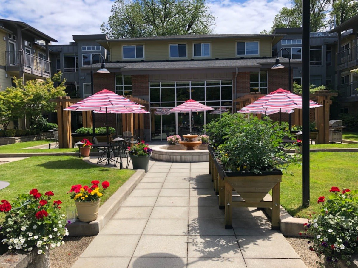 A cozy garden patio with pink umbrellas and vibrant flowers in front of a building.