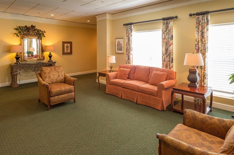 A cozy living room with a sofa, chairs, and lamps arranged on a green carpet.
