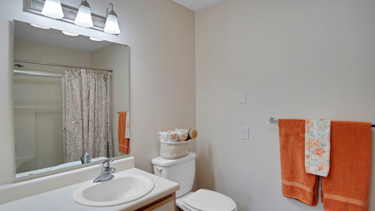 A modern bathroom with a sink, mirror, toilet, and orange towel.