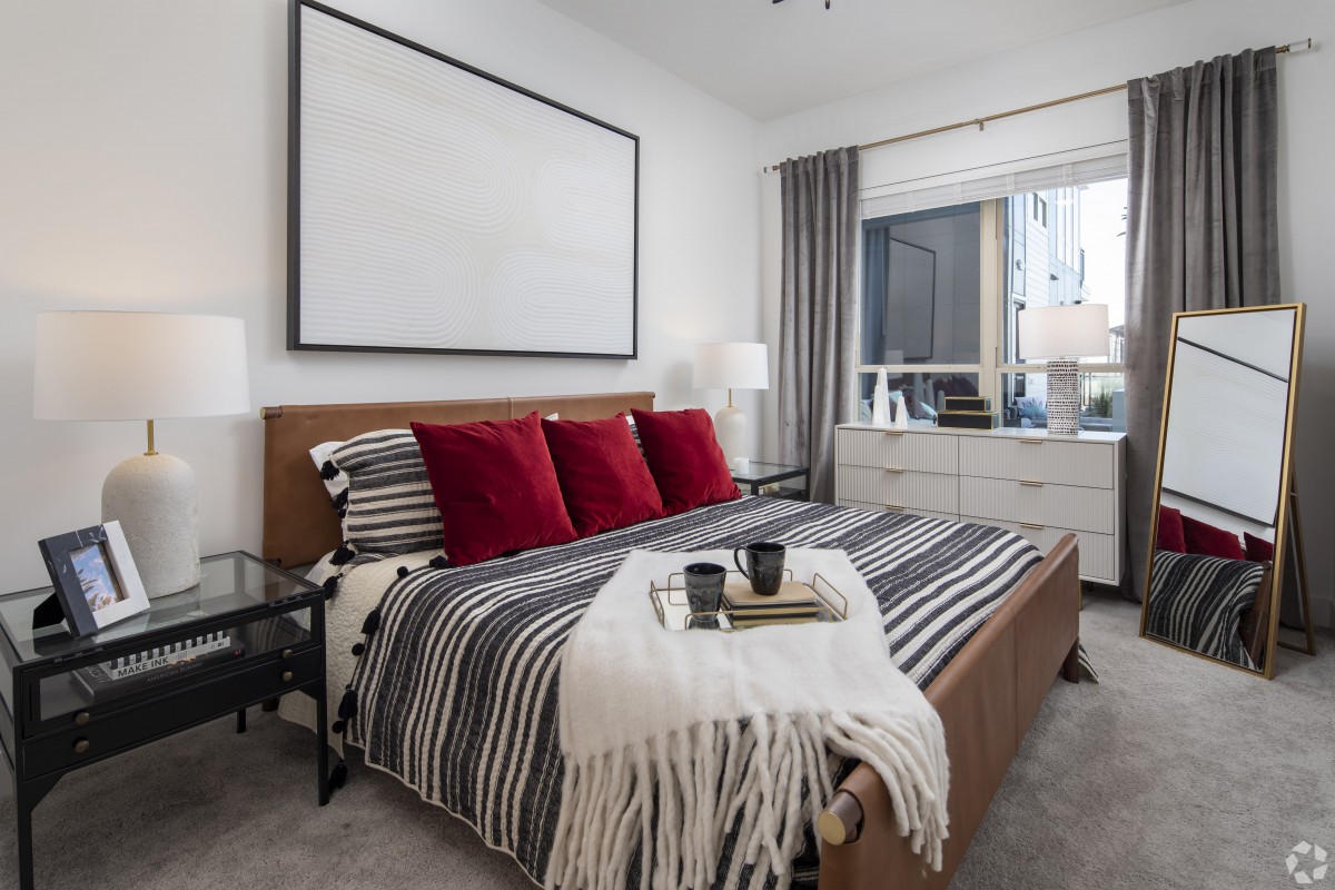 A modern bedroom with a minimalist design featuring a bed adorned with striped bedding and red accent pillows.
