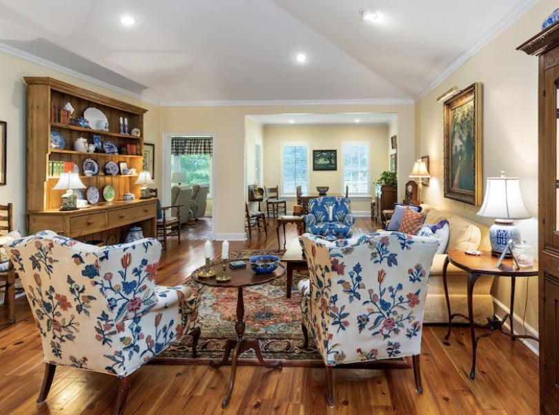 A cozy living room featuring floral-patterned chairs, wooden flooring, and a mix of traditional and decorative elements.