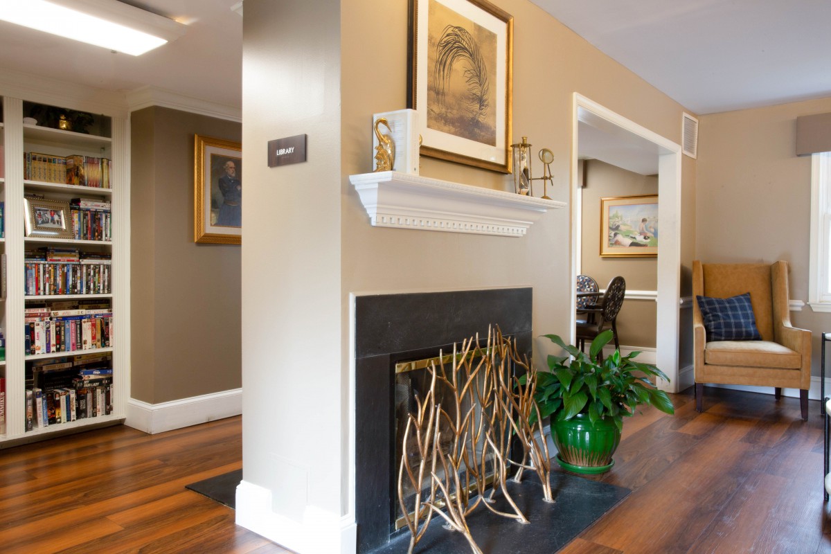 A stylish living room features a decorative fireplace, artwork, and vibrant green plants, complemented by polished wood flooring.