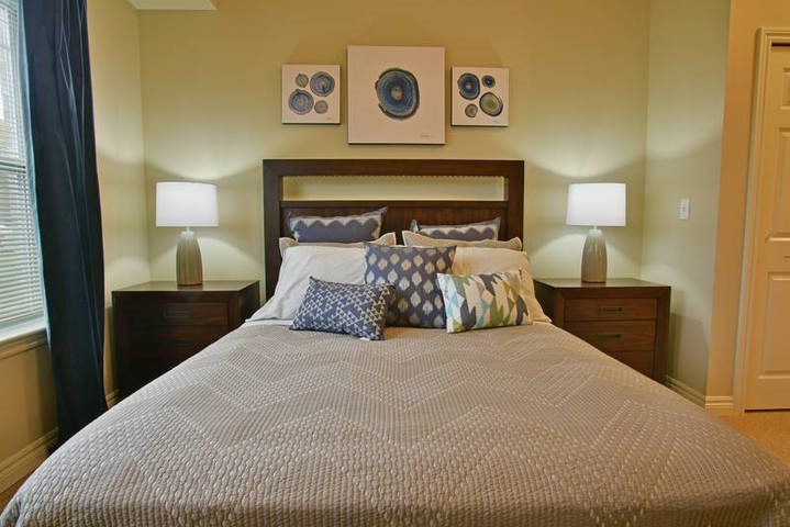 A cozy bedroom with a neatly arranged bed, decorative pillows, two bedside lamps, and artwork on the wall.