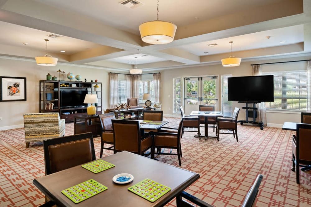 A spacious, well-lit living and dining area with multiple tables, comfortable seating, and large windows providing natural light.