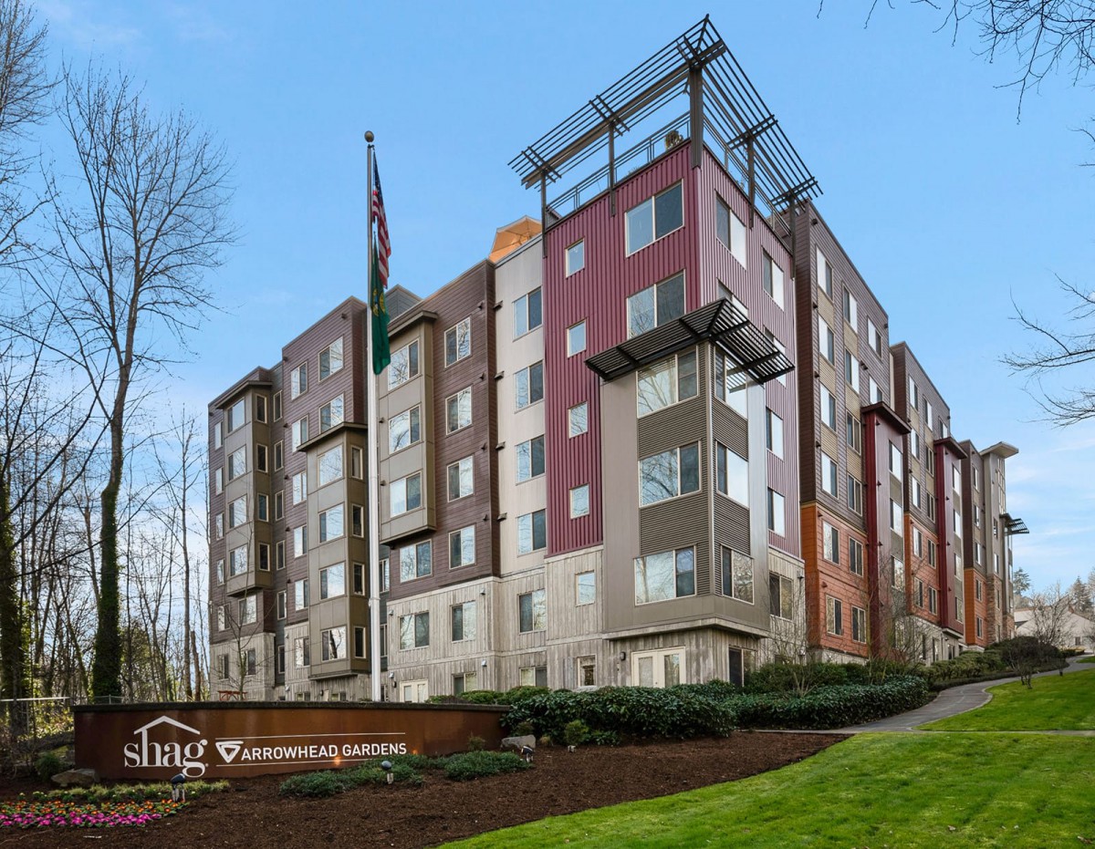 A modern multi-story apartment building set against a clear blue sky.