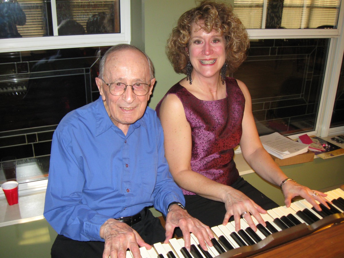 A man and woman smiling while playing the piano together indoors.