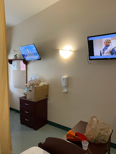 A view of a hospital room featuring two televisions and a dresser.