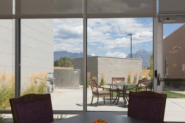 A scenic view of a patio with outdoor seating, framed by a window, showcasing mountains and a cloudy sky in the background.