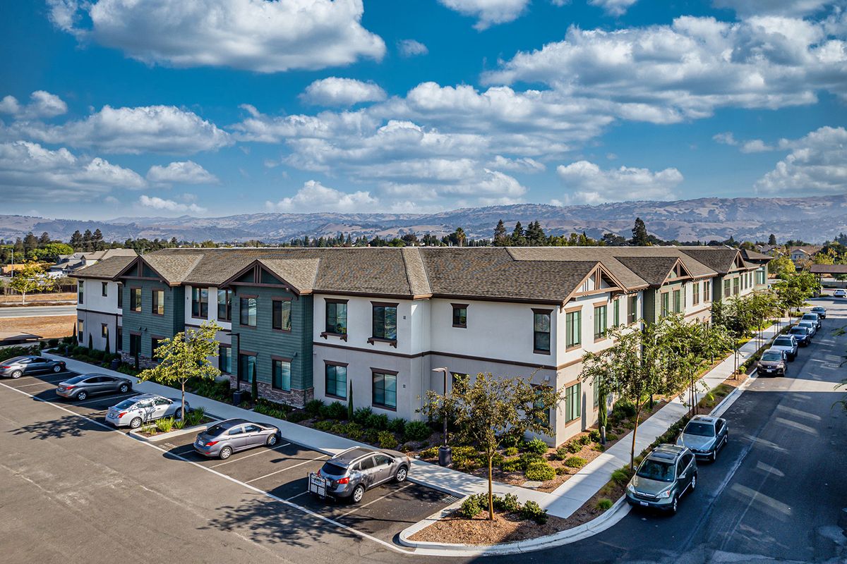 A suburban apartment complex with a parking lot under a partly cloudy sky.
