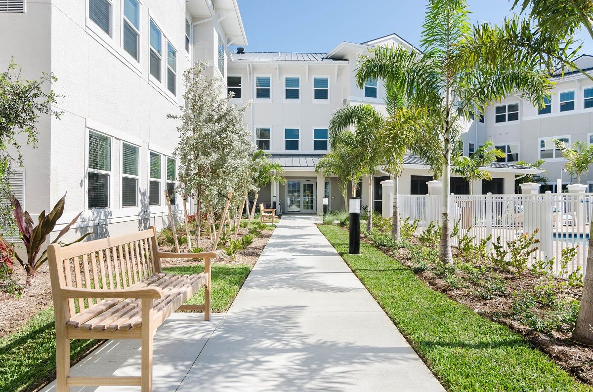 A pathway leading to a modern residential building surrounded by landscaped gardens and palm trees.