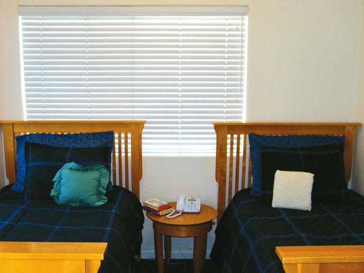A cozy bedroom featuring twin beds with wooden headboards and a central nightstand under window blinds.