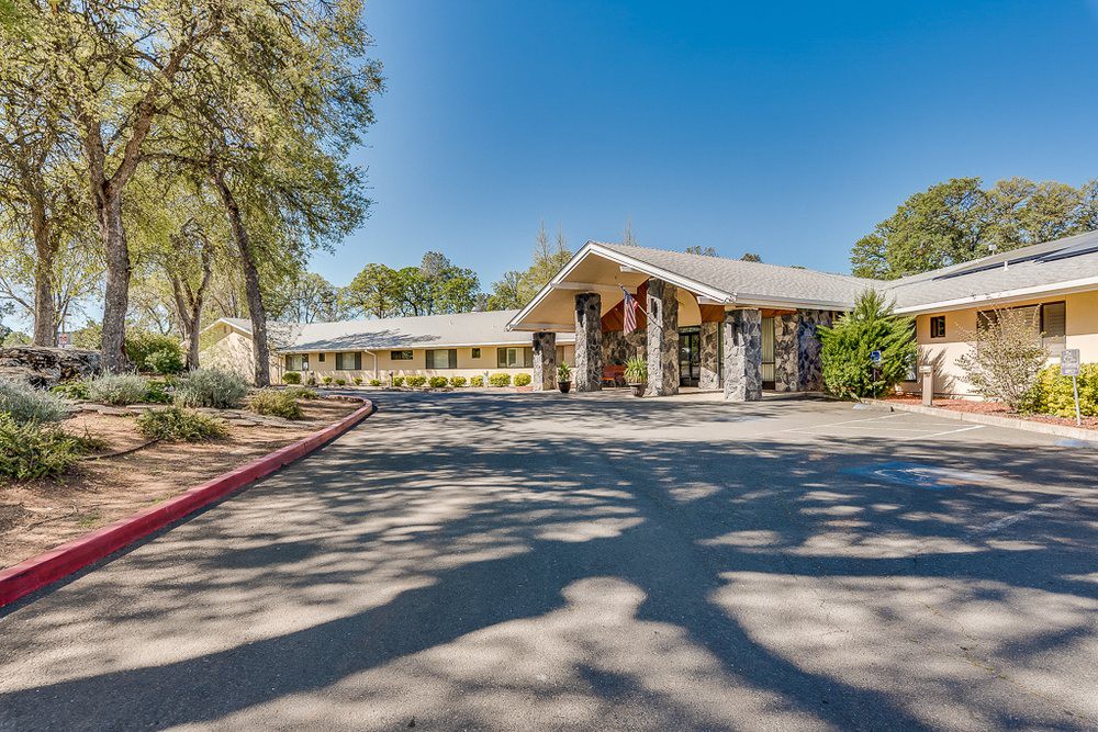 A daytime view of a motel's exterior with a driveway and surrounding trees.