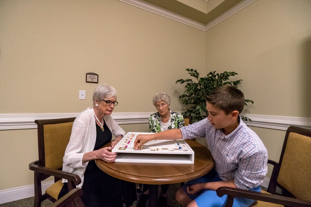 A young person and two elderly individuals play a board game together at a table.