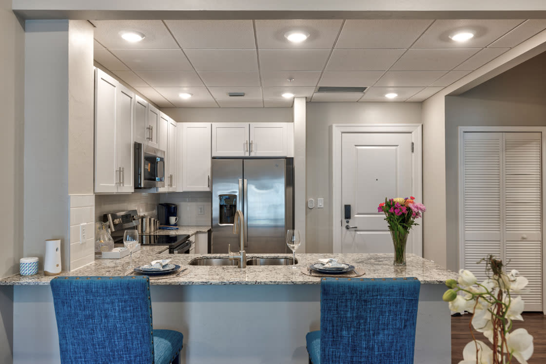 A modern kitchen with a granite countertop, blue bar stools, and stainless steel appliances.