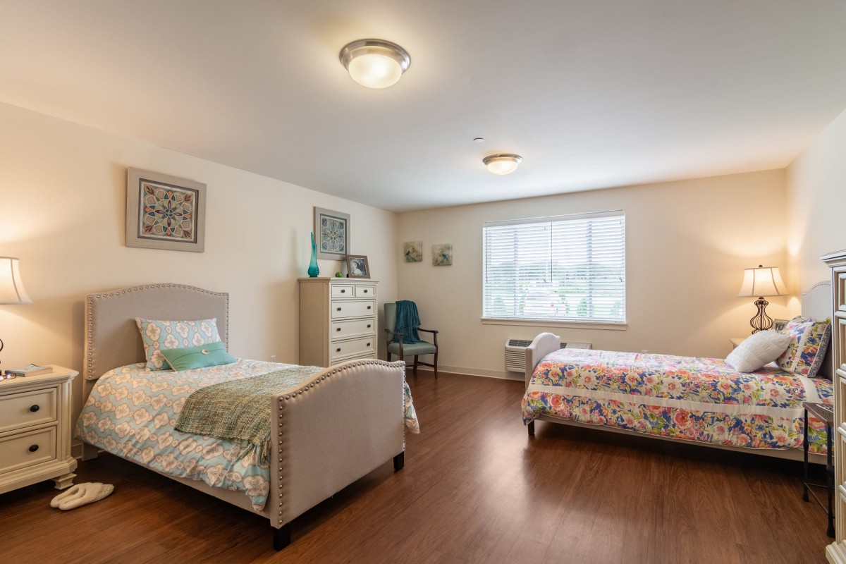 A spacious bedroom with two neatly made single beds, wooden flooring, and a large window allowing natural light.