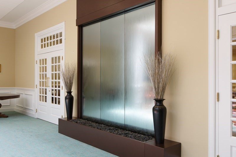 A modern indoor water feature with a waterfall wall, flanked by decorative vases.