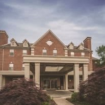 A brick building with a prominent entrance featuring columns and surrounded by trees.