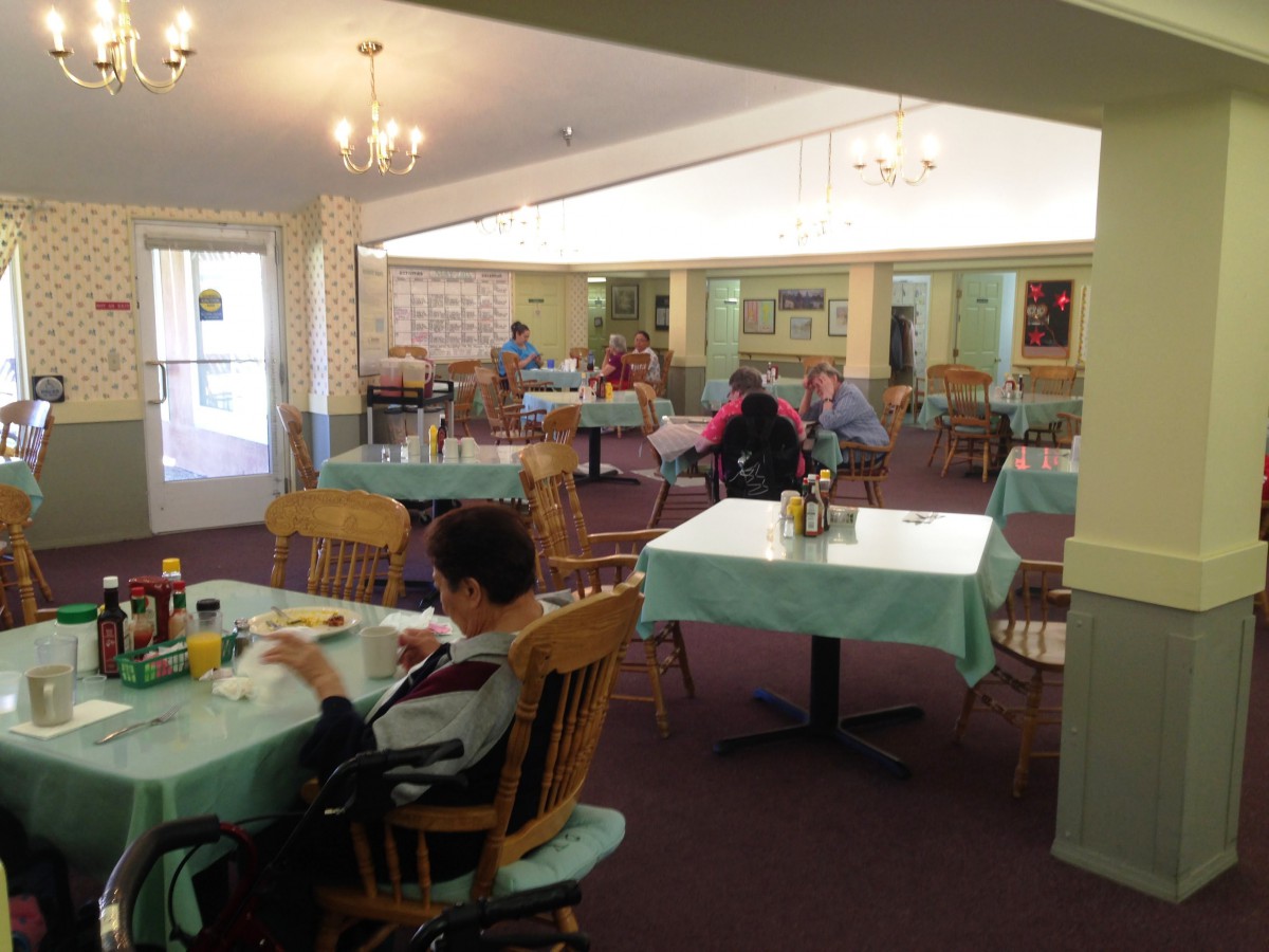 A cozy dining area with several people seated at tables covered with light blue tablecloths.