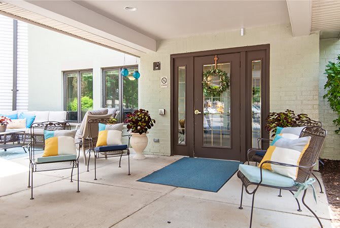 A cozy patio area with cushioned chairs, a decorative wreath on the front door, and potted plants creating an inviting atmosphere.