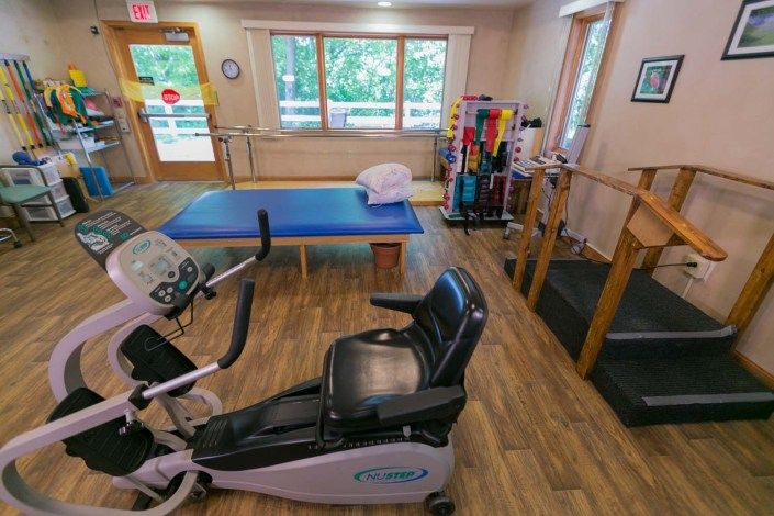 A physical therapy room equipped with an exercise bike, treatment table, and parallel bars.