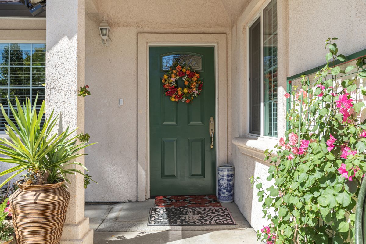 A welcoming green front door adorned with a colorful wreath, surrounded by potted plants.