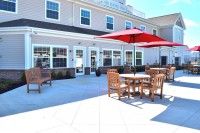 A sunny outdoor patio with tables, chairs, and red umbrellas in front of a building.