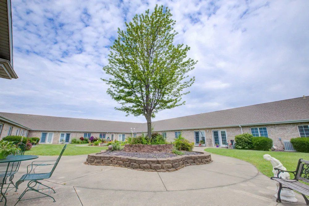 A tree stands in the center of a landscaped courtyard surrounded by buildings under a cloudy sky.