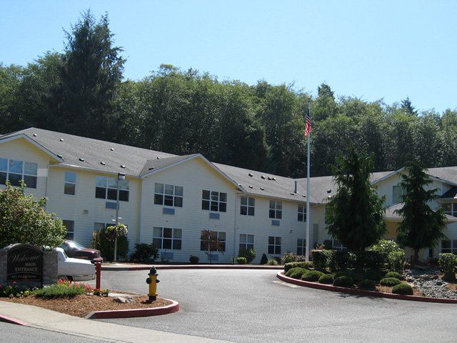 A residential building surrounded by trees and landscaping on a sunny day.