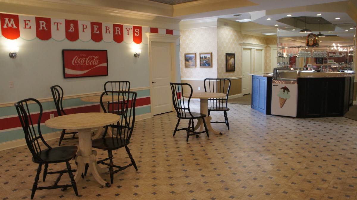 A retro-style diner interior with tables, chairs, and a Coca-Cola sign on the wall.
