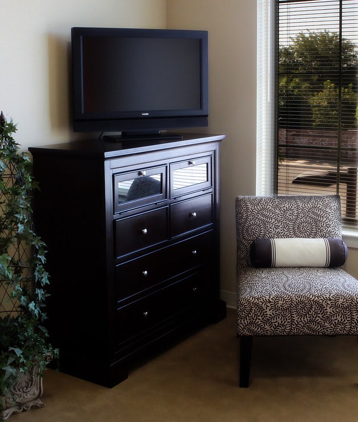 A cozy indoor setup with a television on a dresser and an upholstered chair by the window.