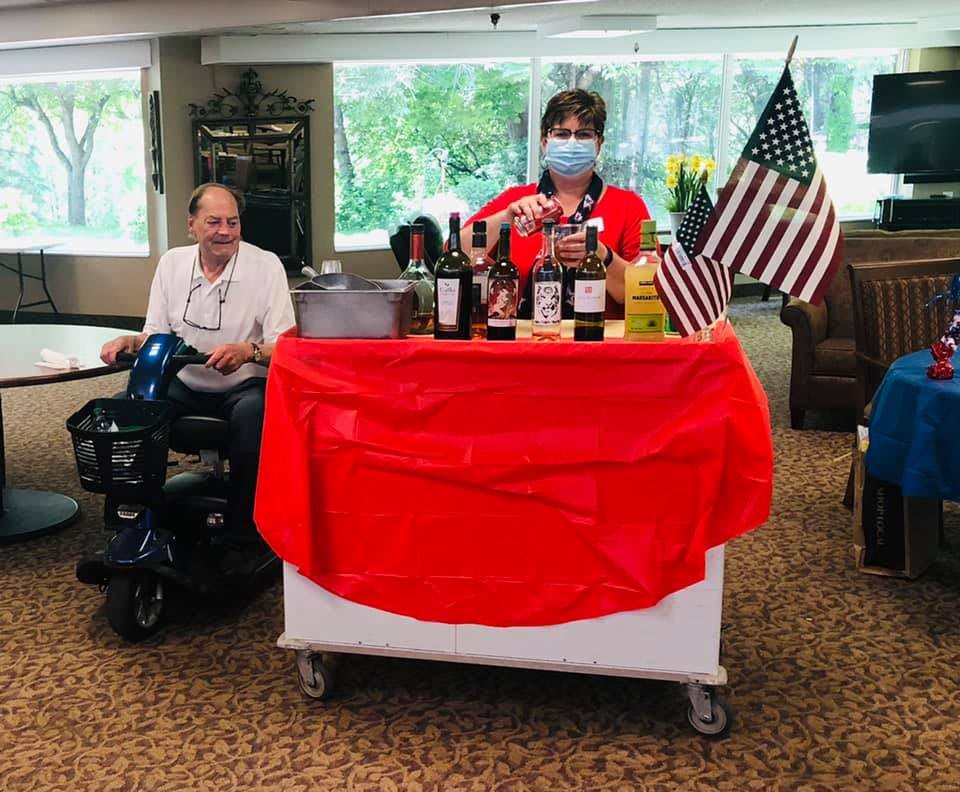 A festive indoor setup with beverages and American flags, featuring a person wearing a mask and another seated nearby.