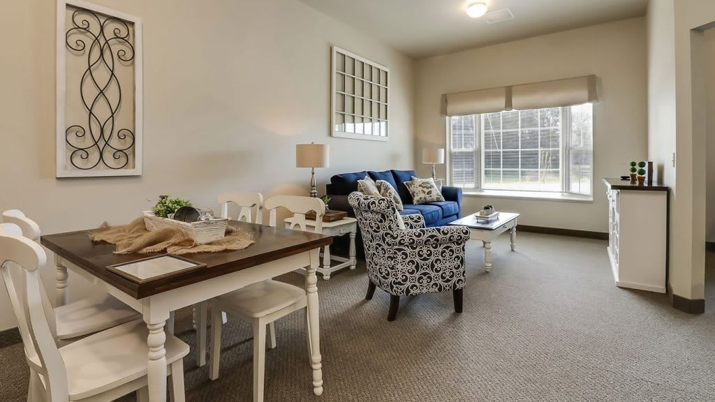 A cozy living room with a dining table, comfortable seating, and ample natural light from a large window.